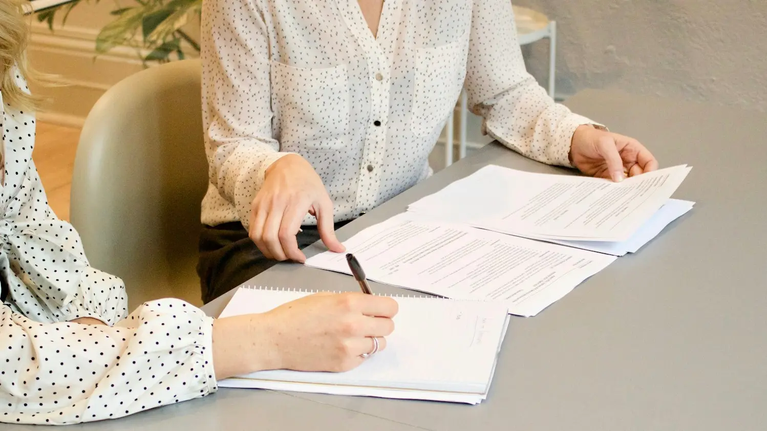 woman signing on white printer paper beside woman about to touch the documents
